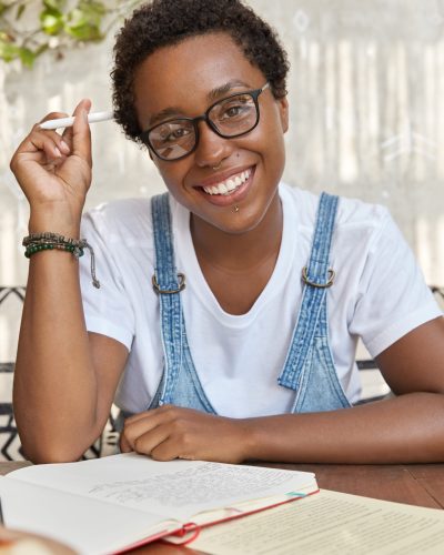 Glad black woman makes few notes in diary, being at good mood, holds pen in hand, reads some information from papers, wears piercing, prepares for business meeting. People, leisure, studying Glad black woman makes few notes in diary, being at good mood, holds pen in hand, reads some information from papers, wears piercing, prepares for business meeting. People, leisure, studying